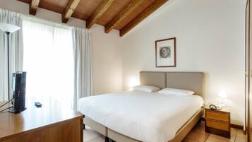 Una camera d'albergo con un letto, un comodino, una lampada e una scrivania con un computer.
