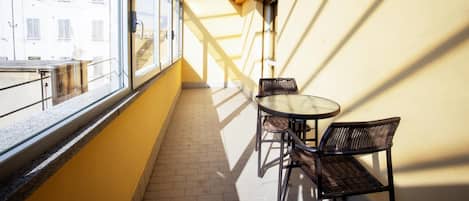 A balcony with a table and chairs, a view of buildings, and a clock on the wall.
