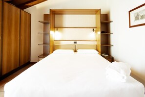 A hotel room with a large bed, wooden wardrobe, and built-in shelves. - Residenza Le Cupole (Parma)