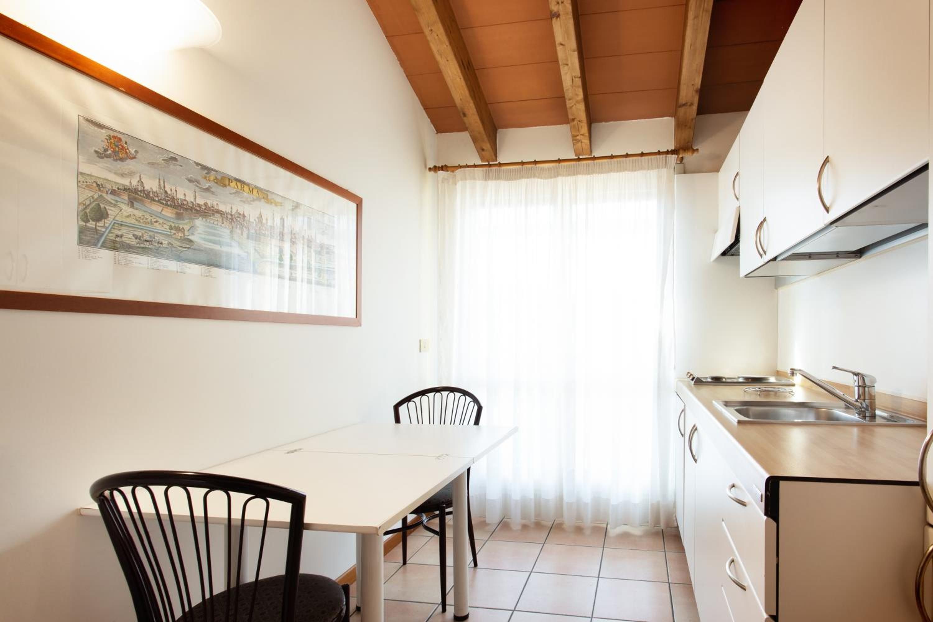 Una piccola cucina con un tavolo da pranzo e sedie, una finestra con tende e un quadro appeso al muro.