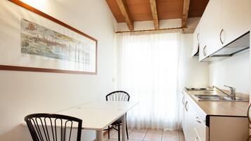 Una piccola cucina con un tavolo da pranzo e sedie, una finestra con tende e un quadro appeso al muro.