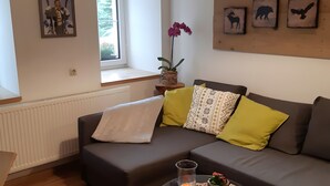 Ein modernes Wohnzimmer mit einem grauen Sofa, gelben und gemusterten Kissen, einem Topf-Orchideen und gerahmten Bildern an der Wand.