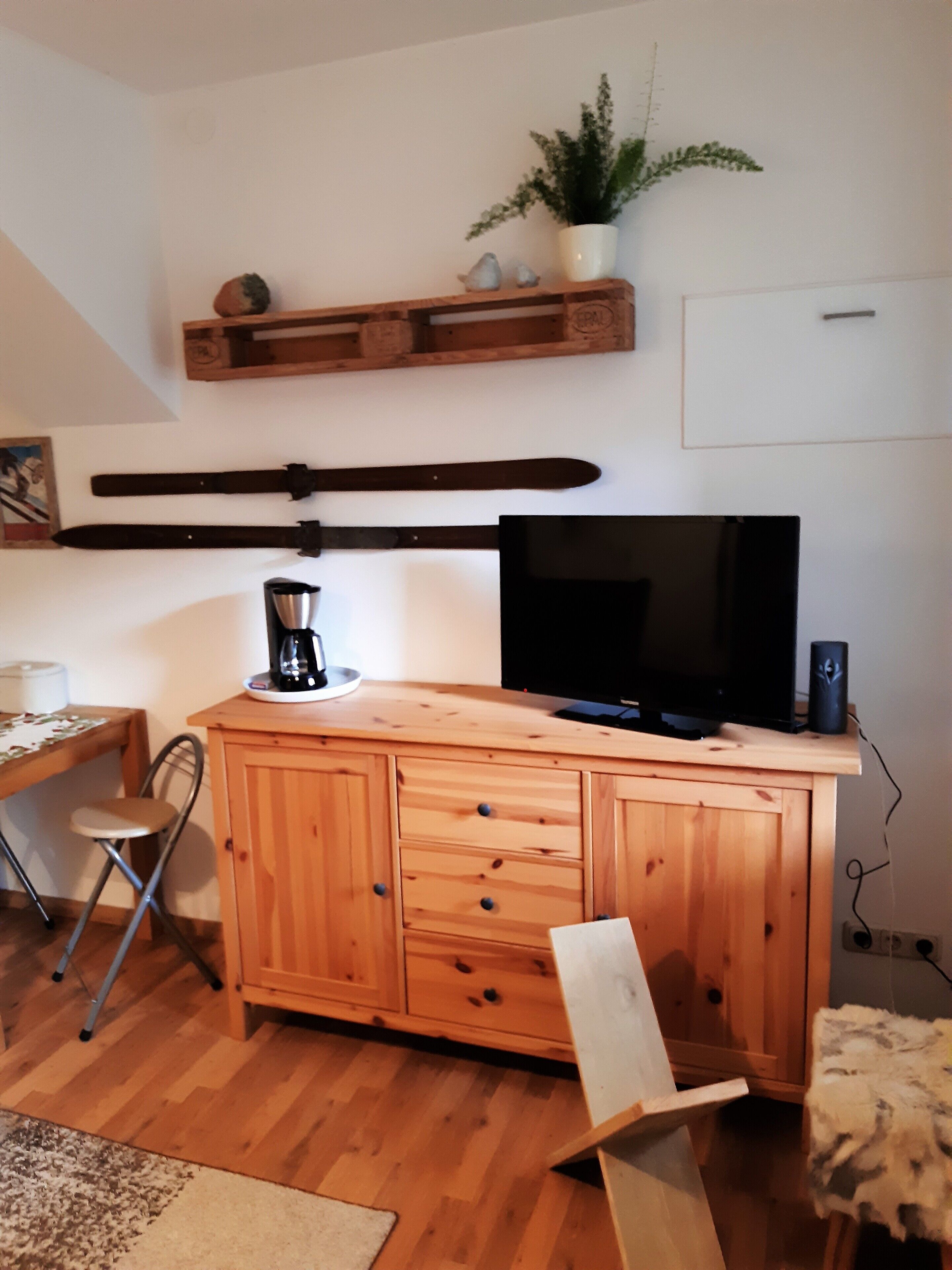 Een houten kast met lades, een televisie, een koffiezetapparaat en een plant aan de muur.
