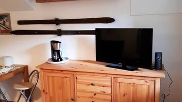Een houten kast met lades, een televisie, een koffiezetapparaat en een plant aan de muur.