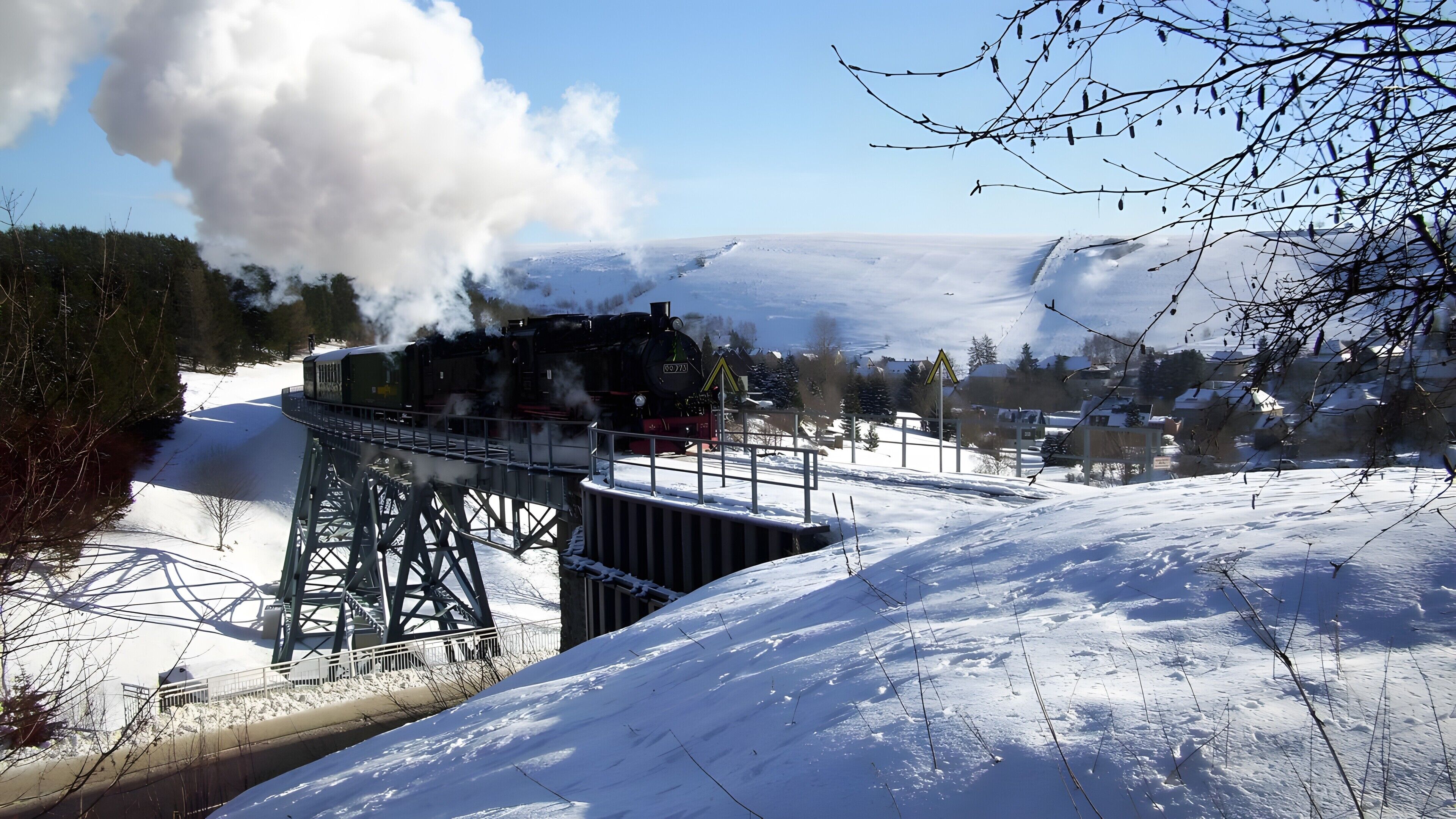 A snow-covered landscape with a steam locomotive on a bridge.