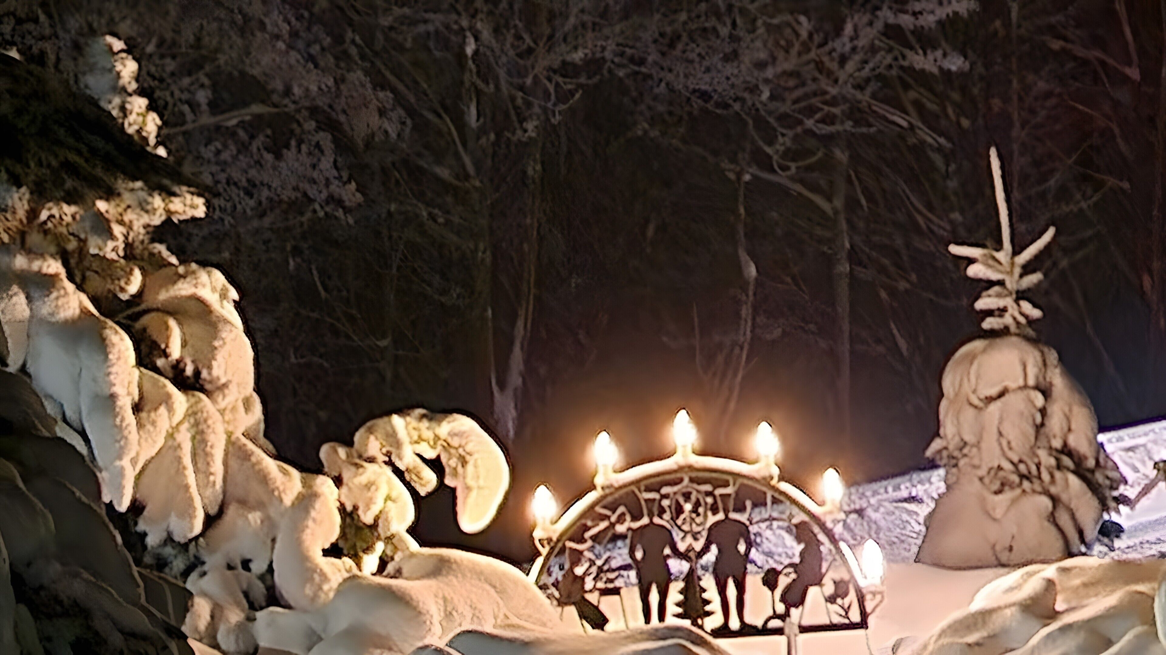 Un espacio exterior cubierto de nieve con una estructura decorativa que presenta velas iluminadas y una figura central.