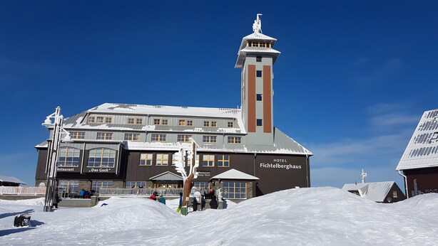 Ein Hotel mit einem markanten Turm, zahlreichen Fenstern und einer verschneiten Umgebung.
