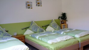 Una habitación con dos camas, ropa de cama verde y una mesita de noche con lámpara.