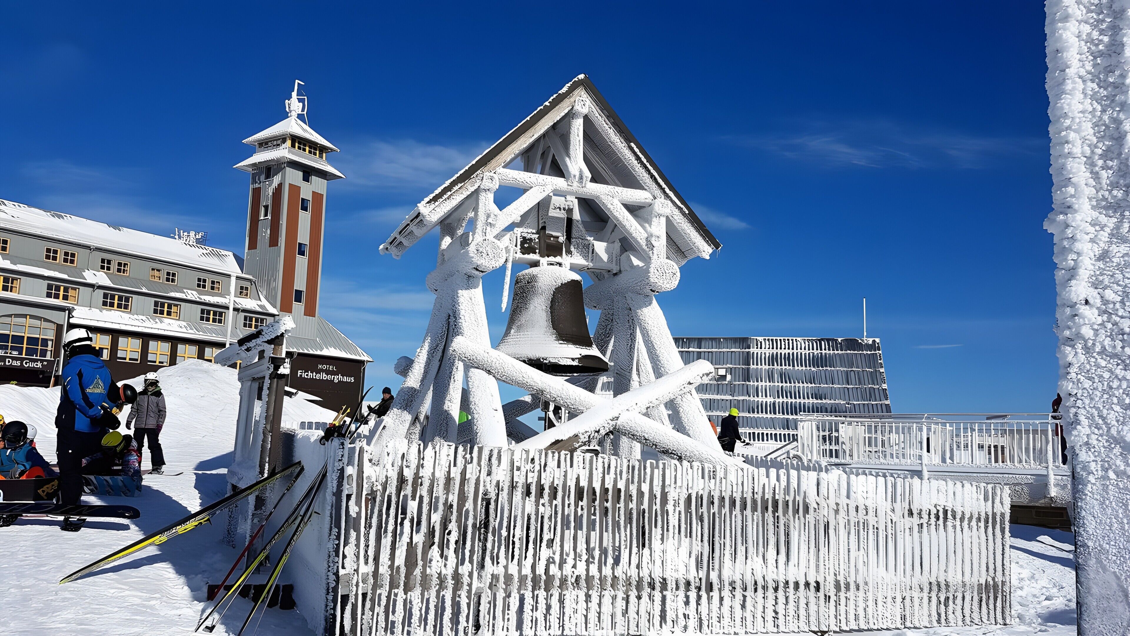 A snow-covered hotel with a bell tower, a ski lift, and a view of a mountain.
