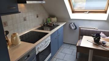 Eine kompakte Küche mit Einbauherd, Backofen und Spüle. Ein kleiner Essbereich mit Tisch und Topfpflanze.