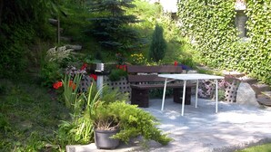 A garden patio with a wooden bench and a table, surrounded by various plants and flowers. - Holiday Apartment for 5 Guests (61 m²) in Oberwiesenthal (Oberwiesenthal)