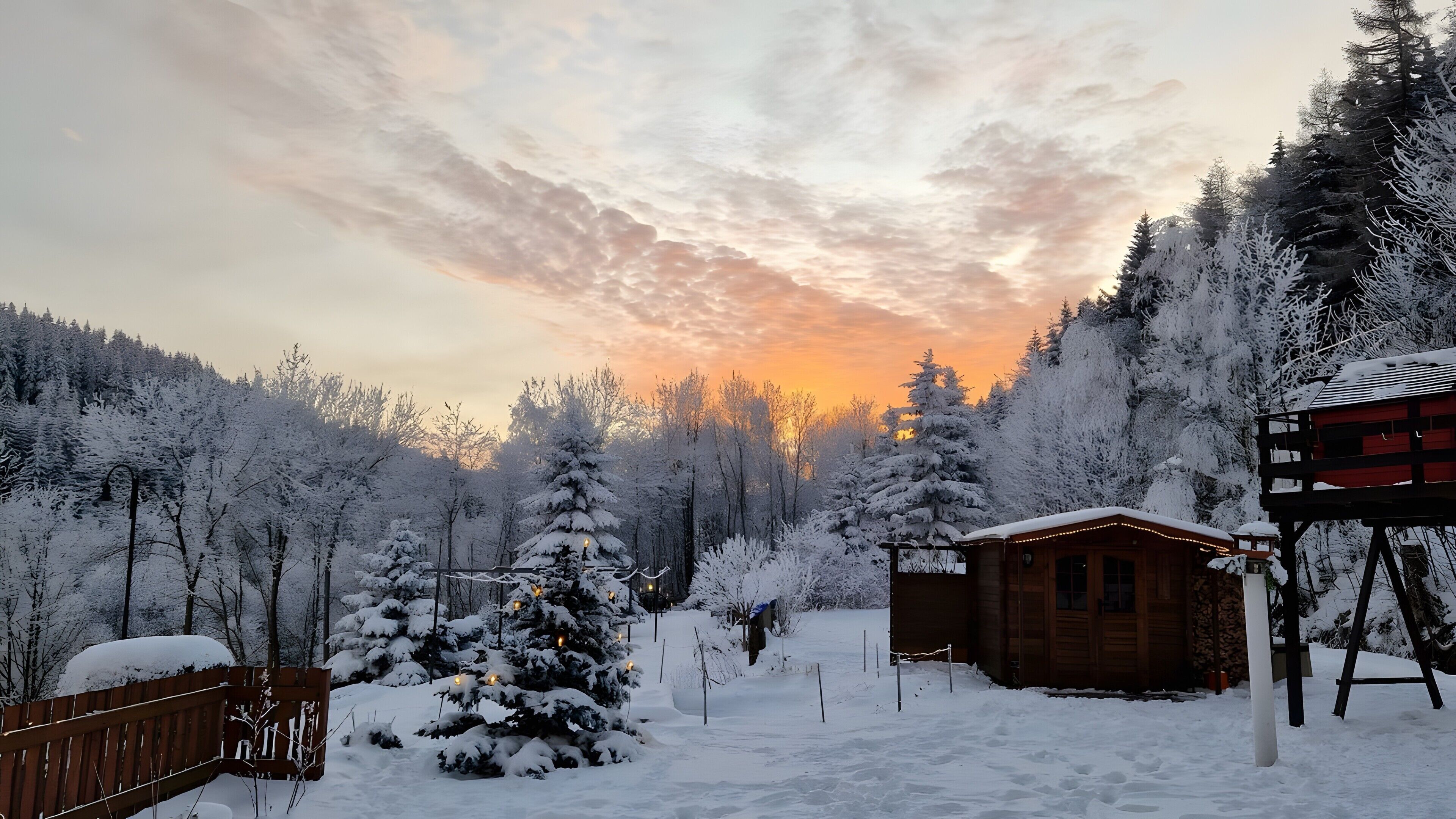 A cabin surrounded by snow-covered trees and a wooden deck.