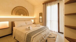 A hotel room with a bed, bedside lamps, a mirror, a window with curtains, and a wooden shelf. - Hotel Baia Tartuga (Stintino)