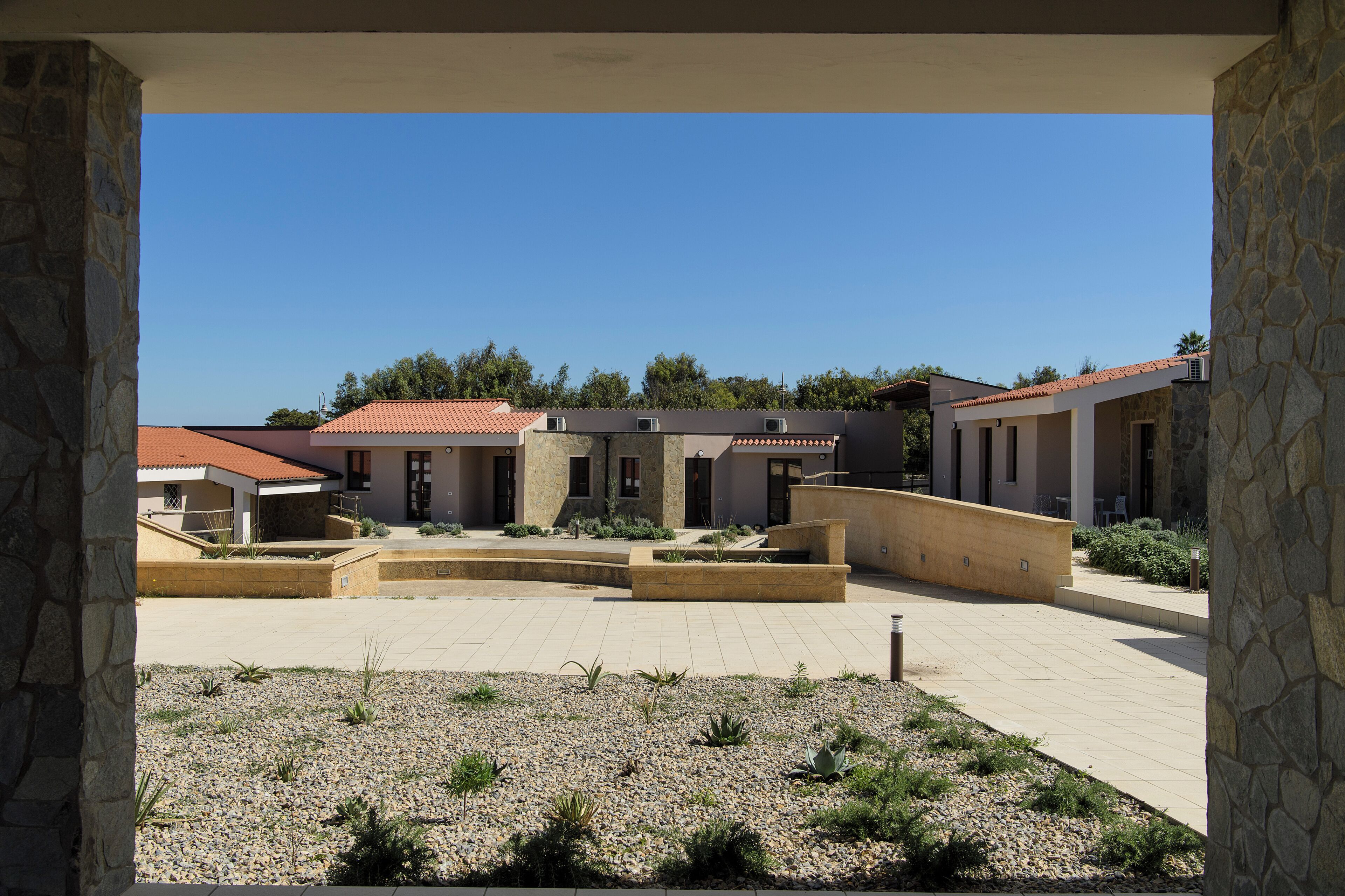 A courtyard with a stone wall, a paved area, and a building with a red-tiled roof.