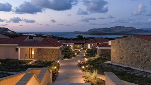 A resort with stone buildings, a paved pathway, and a view of the sea and mountains. - Hotel Baia Tartuga (Stintino)