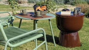 A table with a cup, saucer, and bread, and a camera on a stool, with a view of the sea and mountains in the background. - Hotel Baia Tartuga (Stintino)