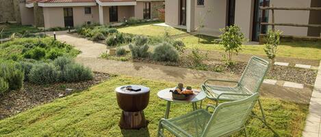 A courtyard with a lawn, a small table with a bowl and a cup, and two green metal chairs.