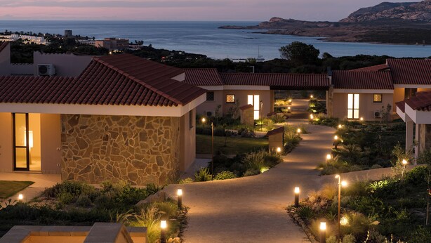 A resort with stone and tiled buildings, a paved pathway, and a view of the sea. - Hotel Baia Tartuga (Stintino)