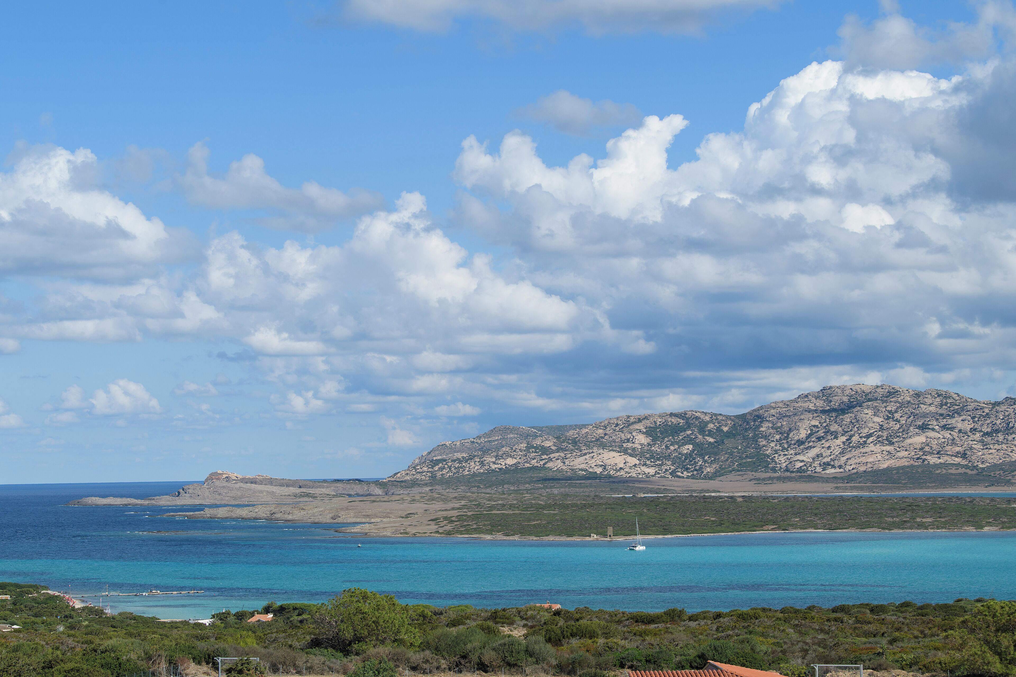 A coastal landscape with a mountain in the background, a clear sky, and a body of water.