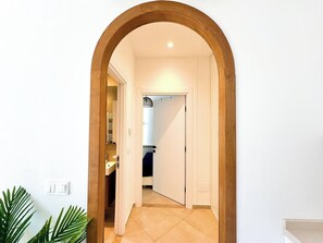 A hallway with a wooden archway leading to a bathroom with a towel rack and a shower. - Appartement Yasmina 1 Bedroom (Sidi Bou Said)