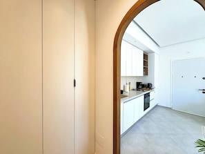 A modern kitchen with white cabinets, a coffee machine, and a view through an archway to a dining area. - Appartement Yasmina 1 Bedroom (Sidi Bou Said)