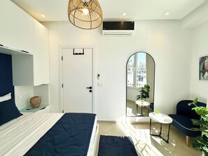 A modern bedroom with a bed, bedside table, hanging light fixture, air conditioning unit, and a view of the outside through a window. - Appartement Yasmina 1 Bedroom (Sidi Bou Said)
