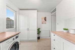 A laundry room with a washing machine, a drying rack, and a window with a view of a wooden fence. - The Derby Nest - Sleeps 6 (Derby)