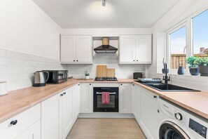 A compact kitchen with white cabinets, a wooden countertop, a built-in oven, a washing machine, and a window with a view of the outside. - The Derby Nest - Sleeps 6 (Derby)