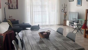 Een eethoek met een houten tafel, stoelen, een bank, een televisie en een raam met gordijnen.