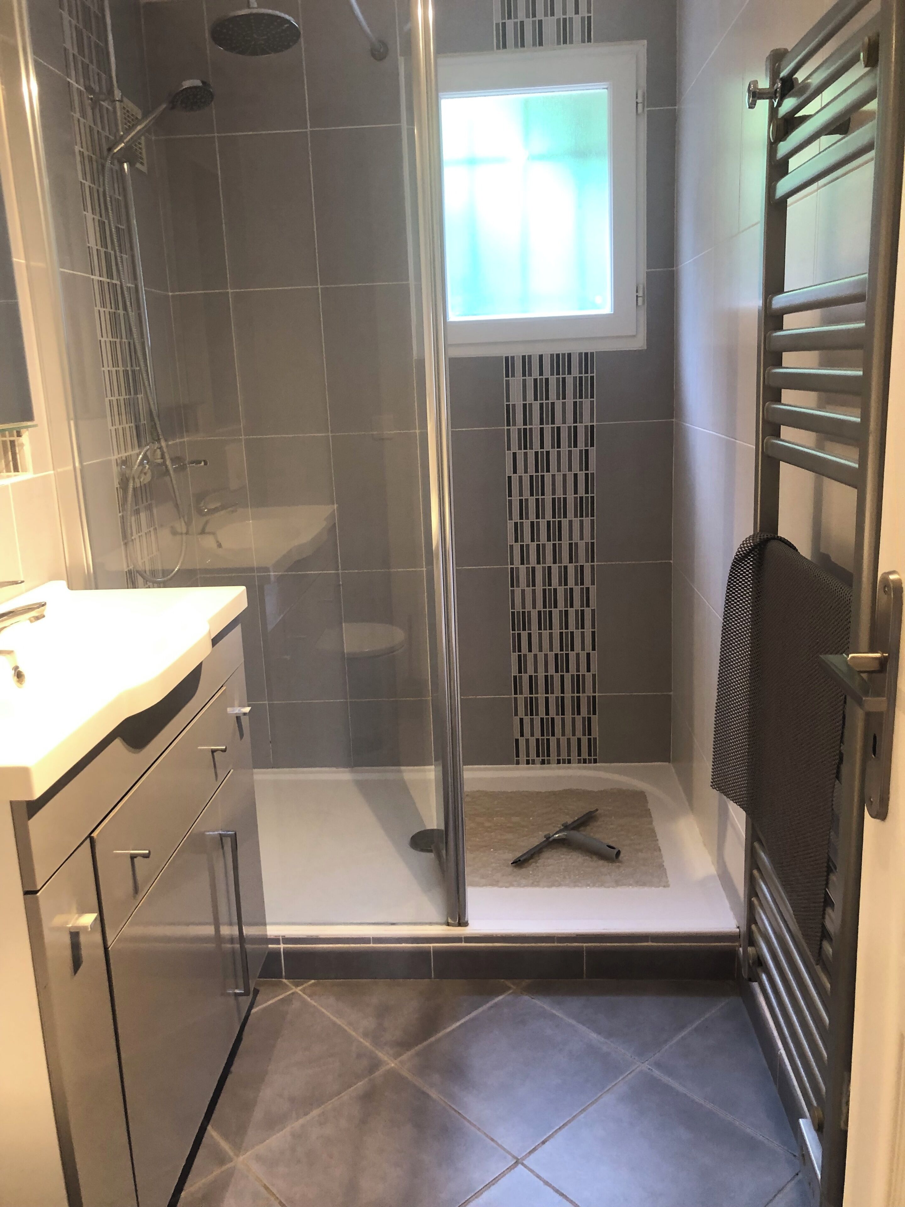 A modern bathroom with a glass shower enclosure, a small window, and a towel rack.