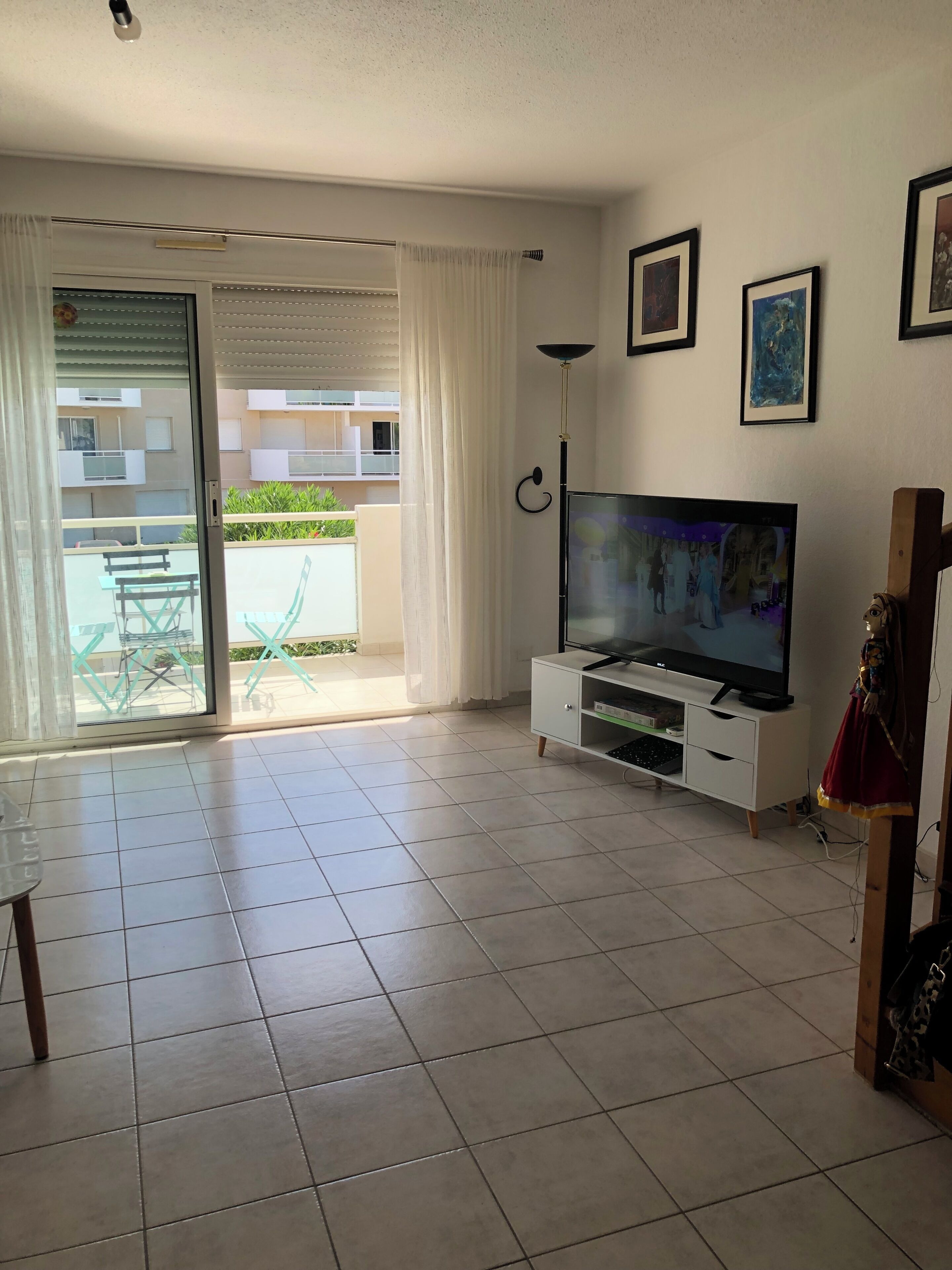 A living room with a flat-screen TV, a white entertainment unit, a dining table with chairs, and a sliding glass door leading to an outdoor area.