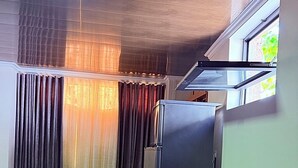 A compact living space with a sofa, a refrigerator, a window with curtains, and a ceiling with a skylight.