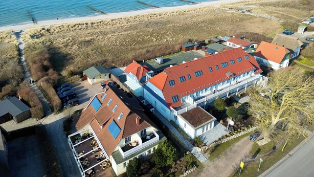 Une vue aérienne d’une propriété située sur la côte, avec plusieurs bâtiments, une plage de sable et une vue dégagée sur la mer.