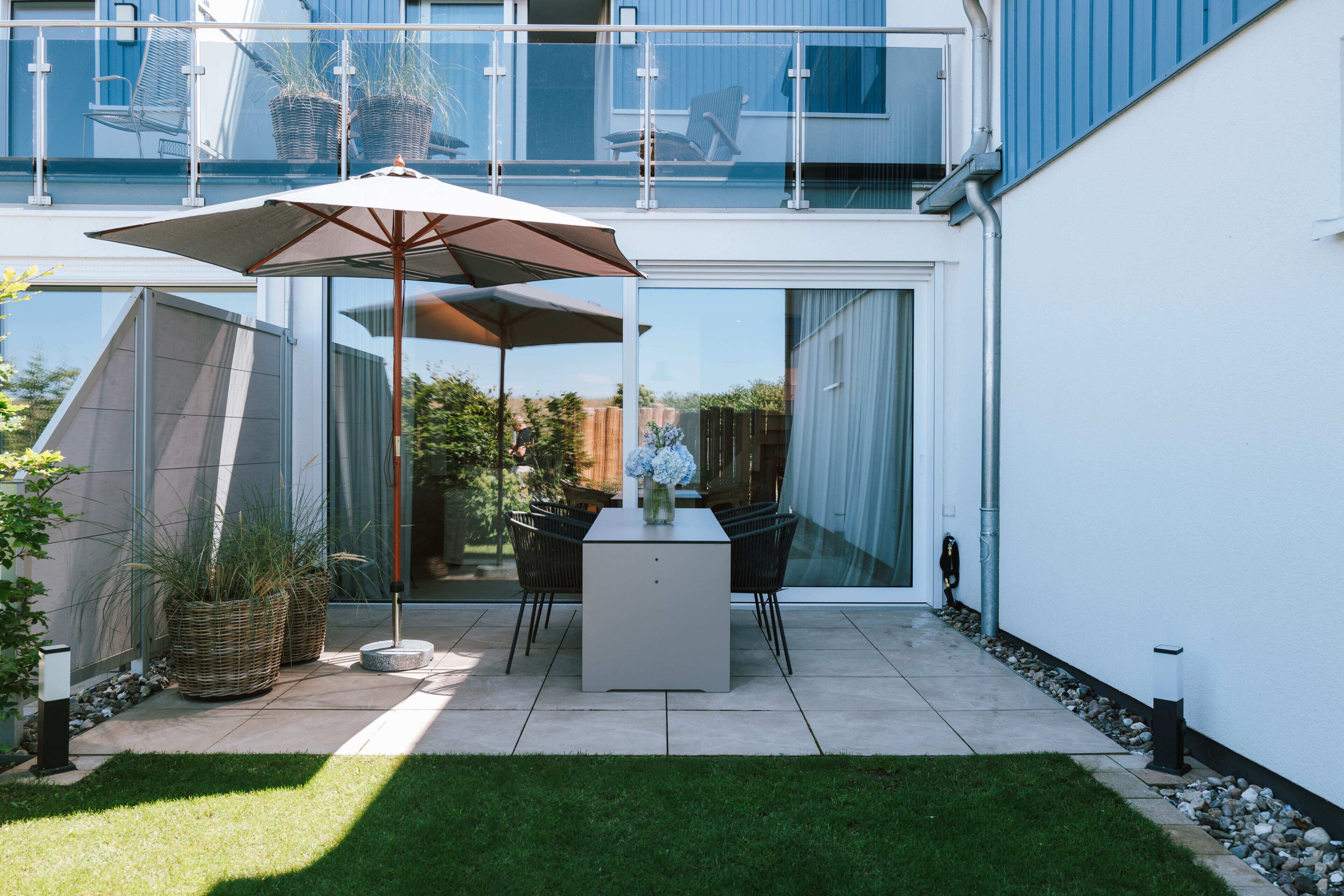 Un patio moderno con una mesa, sillas, un parasol grande y plantas en macetas.