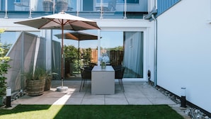 Une terrasse moderne avec une table et des chaises, un grand parasol et des plantes en pot.