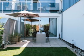 A modern patio with a table and chairs, a large umbrella, and potted plants. - Brand new vacation apartment Weststrand-Blick - Wake up above the Baltic Sea (Ahrenshoop)