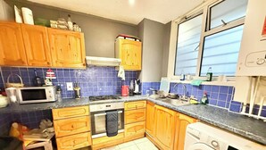 A kitchen with wooden cabinets, a microwave, a stove, a sink, and a washing machine. - Single Occupancy - Lovely Area - 5min to dlr (London)