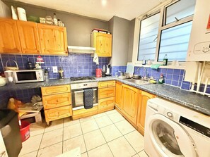 A kitchen with wooden cabinets, a microwave, a stove, a sink, and a washing machine. - Single Occupancy - Lovely Area - 5min to dlr (London)
