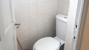 A small, white-tiled bathroom with a toilet and a window above it. - Single Occupancy - Lovely Area - 5min to dlr (London)