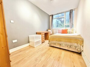 A bedroom with a bed, a wooden dresser, a small white storage unit, and a window with curtains. - Single Occupancy - Lovely Area - 5min to dlr (London)