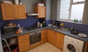 A compact kitchen with wooden cabinets, a microwave, stove, sink, and a washing machine. - Single Occupancy - Lovely Area - 5min to dlr (London)