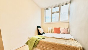 A small, single-bed room with a window, a green throw blanket, and a patterned bedspread. - Single Occupancy - Lovely Area - 5min to dlr (London)