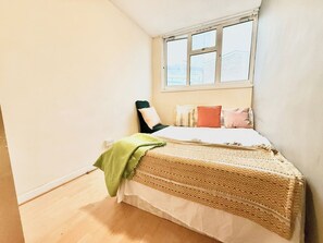 A small, single-bed room with a window, a green throw blanket, and a patterned bedspread. - Single Occupancy - Lovely Area - 5min to dlr (London)