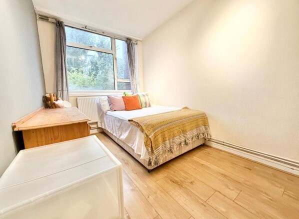 A small, tidy room with a bed, a wooden nightstand, and a white table. - Single Occupancy - Lovely Area - 5min to dlr (London)