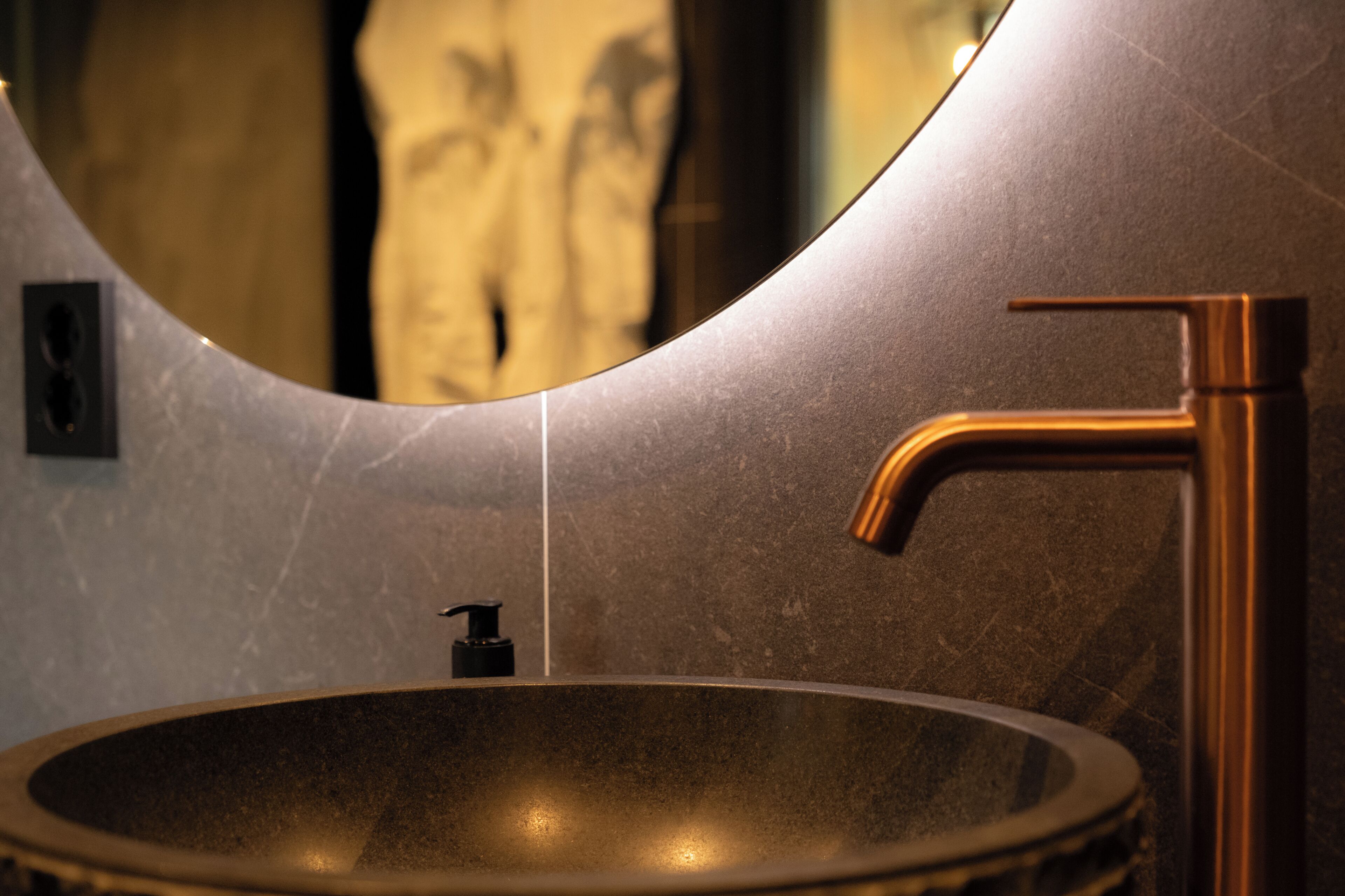 A modern bathroom with a round sink, a faucet, and a mirror.