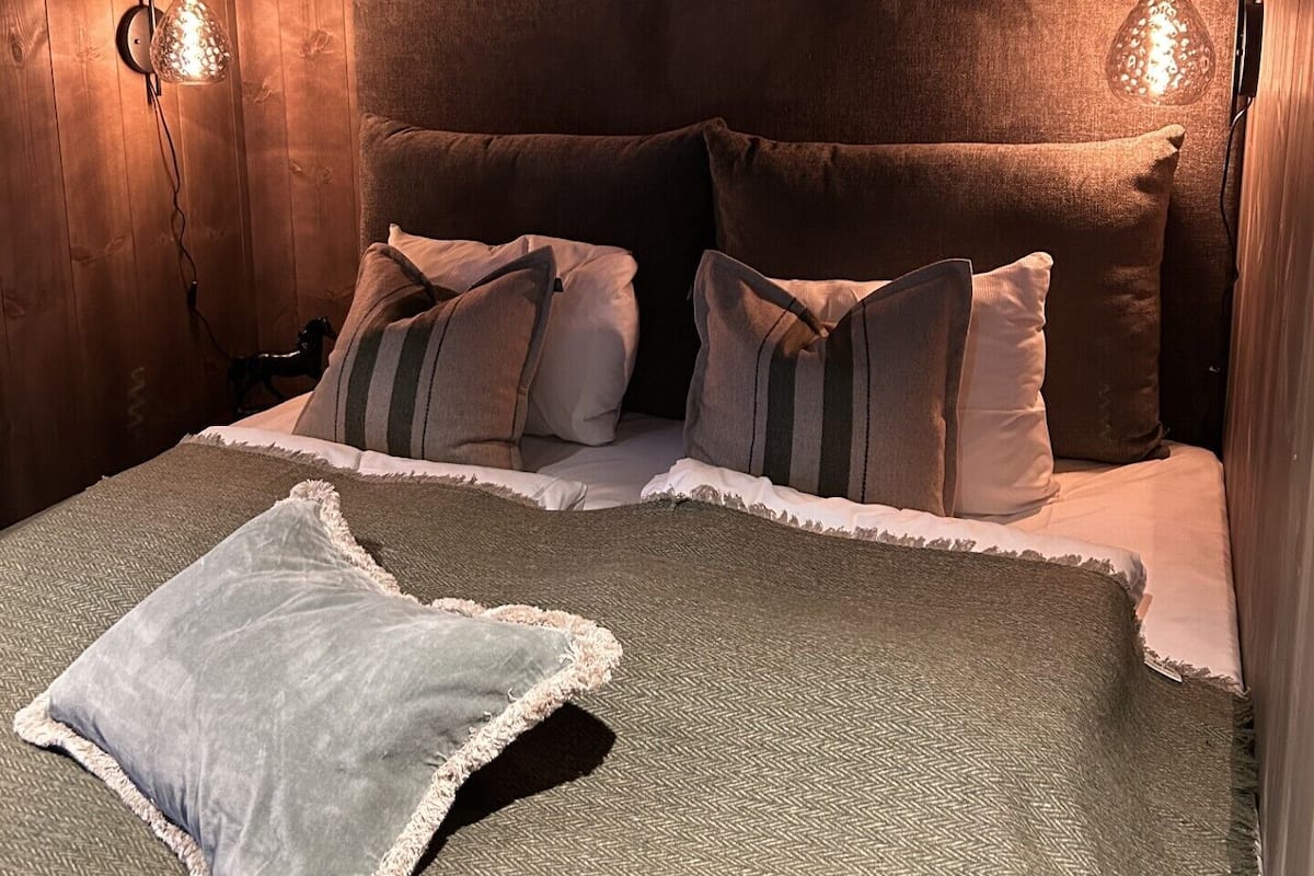 Ein gemütliches Zimmer mit Holzboden, einem Bett mit vielen Kissen und zwei Wandlampen.