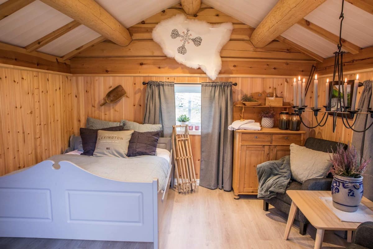Ein Holzblockhaus-Interieur mit einem Bett, einer Couch, einem Tisch und einer Wanddekoration aus Fell.