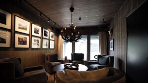 A modern interior with a wooden ceiling, a chandelier, framed pictures on the wall, and a seating area with a round table. - Fjelleventyret (Skjaak)
