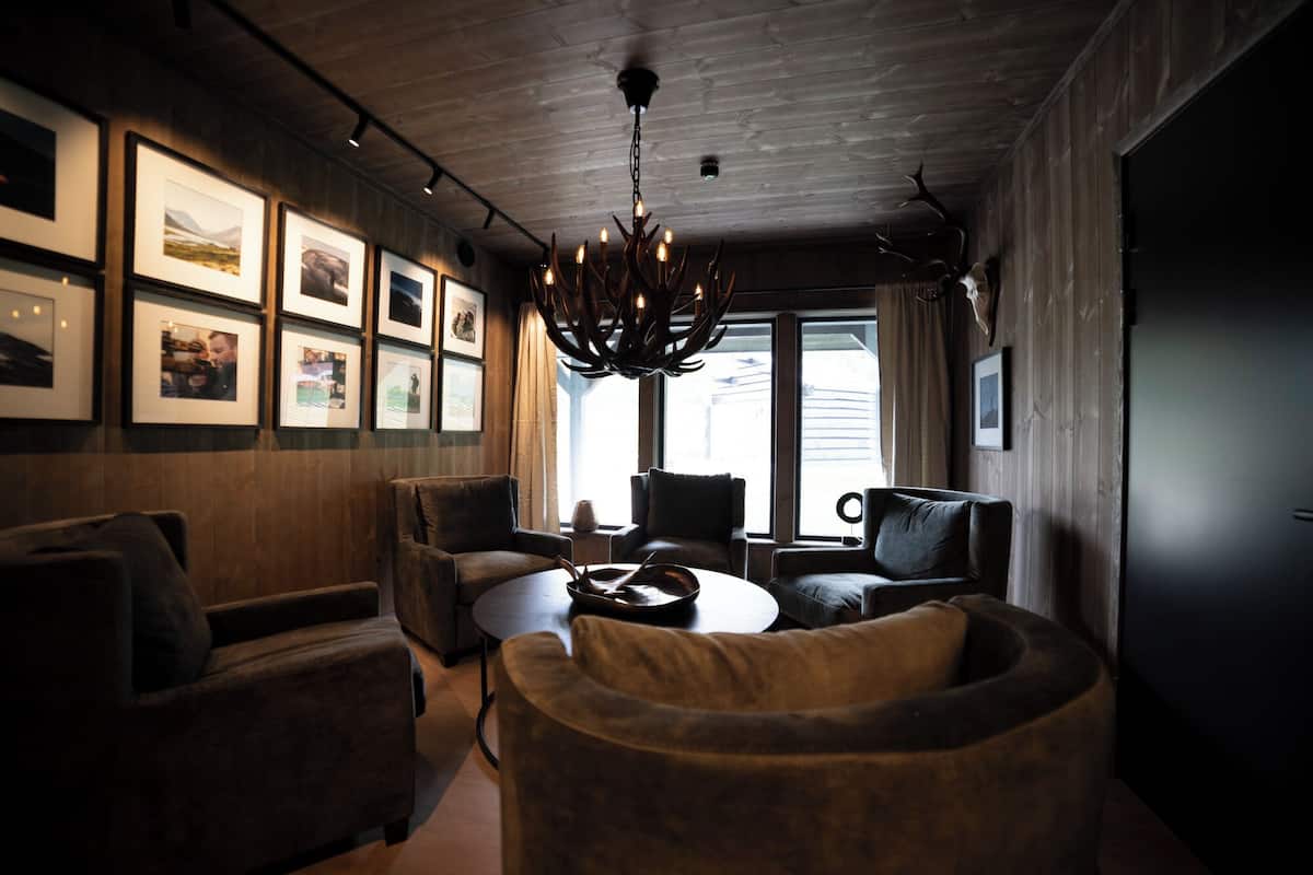 Ein modernes Interieur mit Holzbalkendecke, einer Kristallleuchtre, gerahmten Bildern an der Wand und einer Sitzecke mit rundem Tisch.