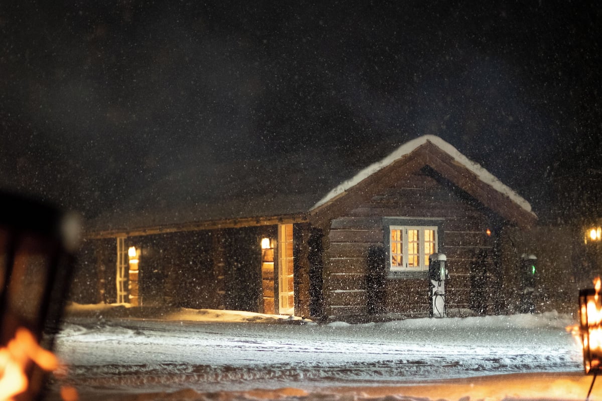 Eine Holzhütte mit verschneitem Gelände, einer sichtbaren Tür und einem Fenster.